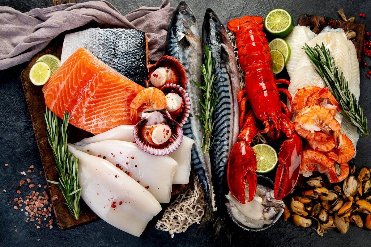 Variety of fresh seafood and herbs arranged on a dark surface, viewed from above